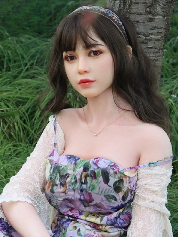 金山薇薇164公分全矽膠娃娃，穿著花卉連身裙，坐在戶外草地上，展現細膩的設計與真實感。