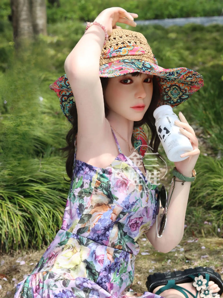 金山全矽膠王薇薇智慧人形，穿著花卉連身裙與草帽，坐在草地上享受戶外生活。